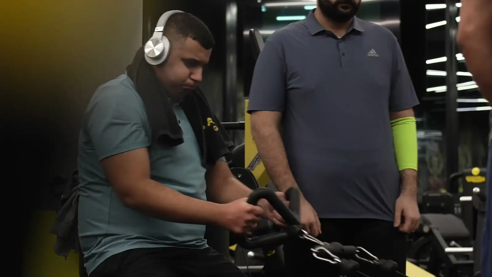 A coach standing beside a client on a cable machine in a gym