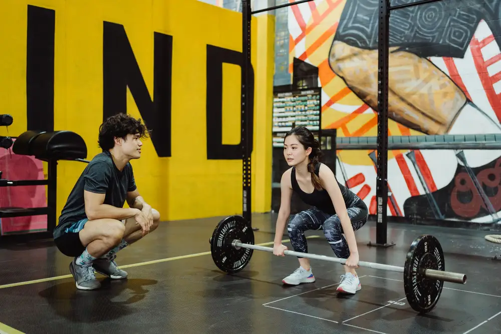 Two people lifting in a gym with a coach nearby